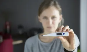 Kobieta z niepokojem trzyma termometr, zastanawiając się, czy zbijać stan podgorączkowy.