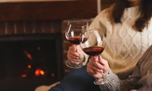 Dwie osoby w ciepłych swetrach wznoszą kieliszki czerwonego wina przy kominku. Czy wino podnosi ciśnienie?