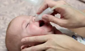 Delikatne odciąganie kataru u niemowlaka za pomocą aspiratora. Dziecko ma otwarte usta, a rodzic ostrożnie wprowadza końcówkę urządzenia do noska.