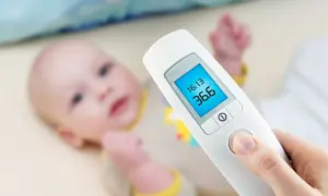 Termometr dla niemowlaka pokazuje 36.6°C. Dziecko leży w tle.