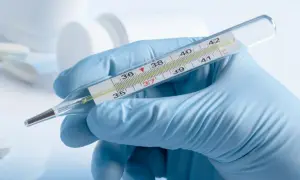Ręka w niebieskiej rękawiczce trzyma termometr. Widać słupek rtęci, który wskazuje temperaturę.
