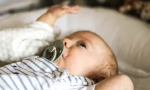 Niemowlę z zielonym smoczkiem, leżące na białej poduszce. Spokojna buzia i lekko uniesiona rączka świadczą o prawidłowej temperaturze u niemowlaka na czole.