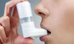 Dłoń trzyma biały inhalator na astmę, który osoba wkłada do ust.