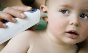 Dziecko z niebieskimi oczami ma mierzoną temperaturę w uchu.