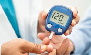 Glukometr na rękę pokazuje wynik 120 mg/dL. Osoba wykonuje pomiar cukru we krwi.