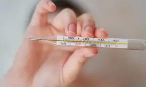 Dłoń trzyma termometr, pokazując, jak zmierzyć temperaturę. Widoczna jest skala od 35 do 42 stopni Celsjusza.