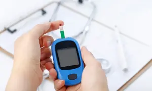 Ręka z kroplą krwi na pasku testowym glukometru, gotowa do badania cukru. W tle stetoskop i dokumentacja medyczna.