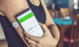 Osoba sprawdza na telefonie wykres poziomu glukozy. Glukometr pokazuje 105 mg/dL, ale nie widać, czy wynik jest prawidłowy.