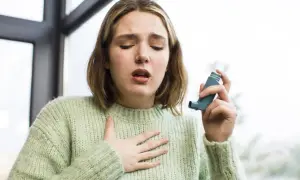 Młoda kobieta z nieleczoną alergią wziewną łapie oddech, trzymając inhalator.