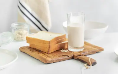 Kanapki z białego pieczywa i szklanka mleka na desce. Czy w mleku jest gluten? Pytanie o składniki śniadania.
