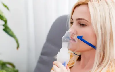 Kobieta z maską inhalacyjną na twarzy. Choć inhalacje solą fizjologiczną są bezpieczne, warto znać potencjalne skutki uboczne.