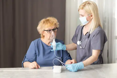 Pielęgniarka pomaga starszej kobiecie z maską inhalacyjną. Dowiedz się, jak zrobić inhalacje z soli fizjologicznej bez inhalatora.