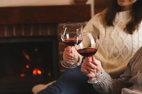 Dwie osoby w ciepłych swetrach wznoszą kieliszki czerwonego wina przy kominku. Czy wino podnosi ciśnienie?