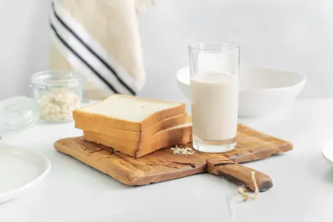 Kanapki z białego pieczywa i szklanka mleka na desce. Czy w mleku jest gluten? Pytanie o składniki śniadania.