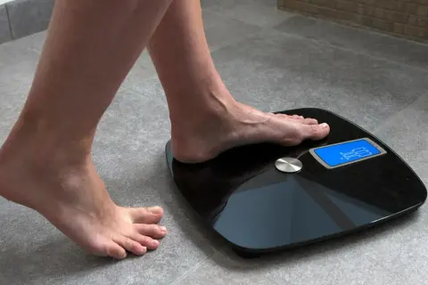 Kobieta stawia stopę na wadze elektronicznej, by sprawdzić, jak się ważyć. Wynik 62.5 kg.