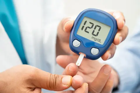 Glukometr na rękę pokazuje wynik 120 mg/dL. Osoba wykonuje pomiar cukru we krwi.