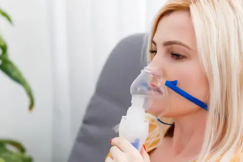 Kobieta z maską inhalacyjną na twarzy. Choć inhalacje solą fizjologiczną są bezpieczne, warto znać potencjalne skutki uboczne.