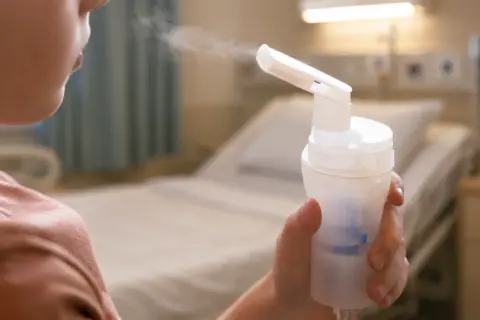Dziecko wdycha lek przez komorę inhalacyjną dla dzieci w szpitalnym pokoju.