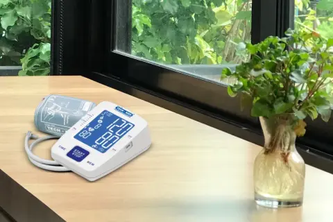 Cyfrowe symbole na ciśnieniomierzu TECH-MED pokazują odczyt 120/80. Obok leży mankiet.