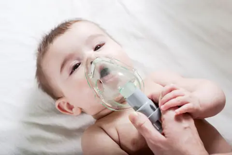 Niemowlę przechodzi nebulizację, czyli formę inhalacji, z maską na twarzy.