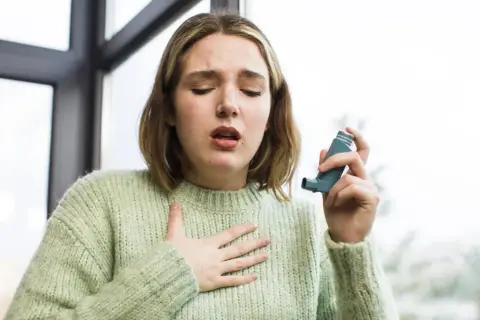 Młoda kobieta z nieleczoną alergią wziewną łapie oddech, trzymając inhalator.