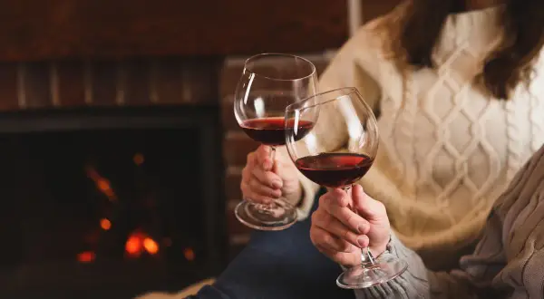 Dwie osoby w ciepłych swetrach wznoszą kieliszki czerwonego wina przy kominku. Czy wino podnosi ciśnienie?