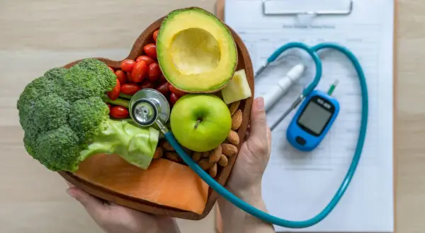 Serce pełne zdrowych produktów: łosoś, brokuły, awokado, jabłko, pomidorki, migdały i ser. Stetoskop i glukometr sugerują dietę glikemiczną.
