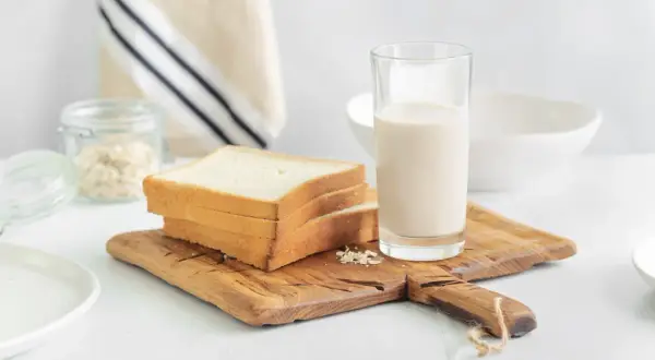 Kanapki z białego pieczywa i szklanka mleka na desce. Czy w mleku jest gluten? Pytanie o składniki śniadania.