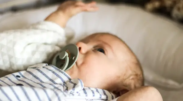 Niemowlę z zielonym smoczkiem, leżące na białej poduszce. Spokojna buzia i lekko uniesiona rączka świadczą o prawidłowej temperaturze u niemowlaka na czole.