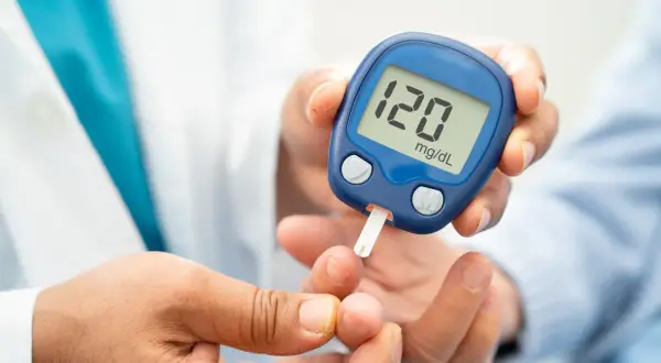 Glukometr na rękę pokazuje wynik 120 mg/dL. Osoba wykonuje pomiar cukru we krwi.
