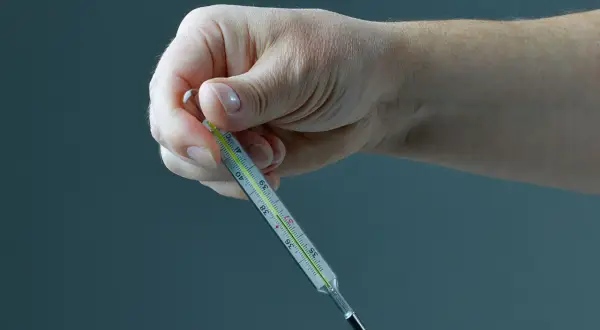 Dłoń trzyma termometr, na którym widać cienką, srebrzystą linię rtęci sięgającą do około 37,5°C.