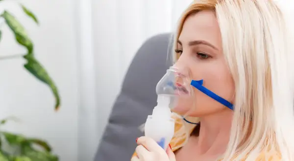 Kobieta z maską inhalacyjną na twarzy. Choć inhalacje solą fizjologiczną są bezpieczne, warto znać potencjalne skutki uboczne.