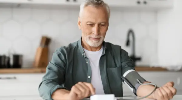 Starszy mężczyzna zaniepokojony, dlaczego holter ciśnieniowy nie pompuje. Sprawdza urządzenie, by dowiedzieć się, co jest przyczyną problemu.