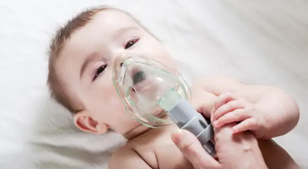 Niemowlę przechodzi nebulizację, czyli formę inhalacji, z maską na twarzy.