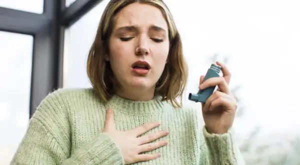 Młoda kobieta z nieleczoną alergią wziewną łapie oddech, trzymając inhalator.