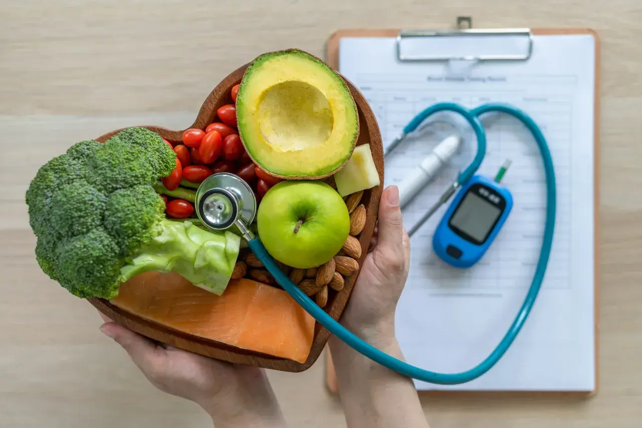 Serce pełne zdrowych produktów: łosoś, brokuły, awokado, jabłko, pomidorki, migdały i ser. Stetoskop i glukometr sugerują dietę glikemiczną.
