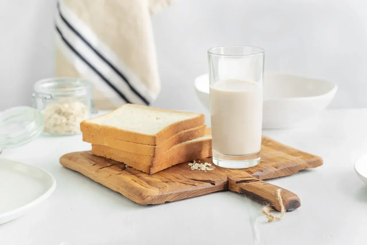 Kanapki z białego pieczywa i szklanka mleka na desce. Czy w mleku jest gluten? Pytanie o składniki śniadania.