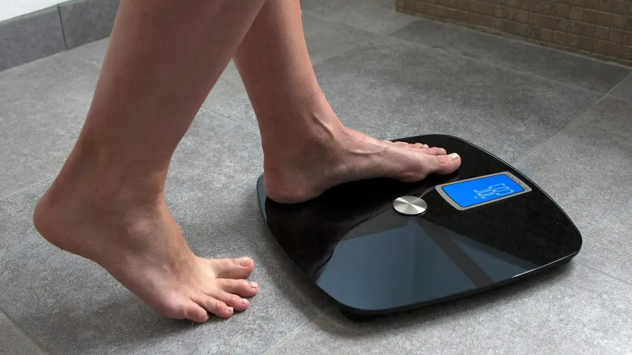 Kobieta stawia stopę na wadze elektronicznej, by sprawdzić, jak się ważyć. Wynik 62.5 kg.