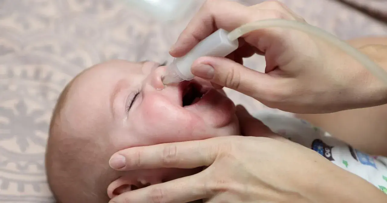Delikatne odciąganie kataru u niemowlaka za pomocą aspiratora. Dziecko ma otwarte usta, a rodzic ostrożnie wprowadza końcówkę urządzenia do noska.