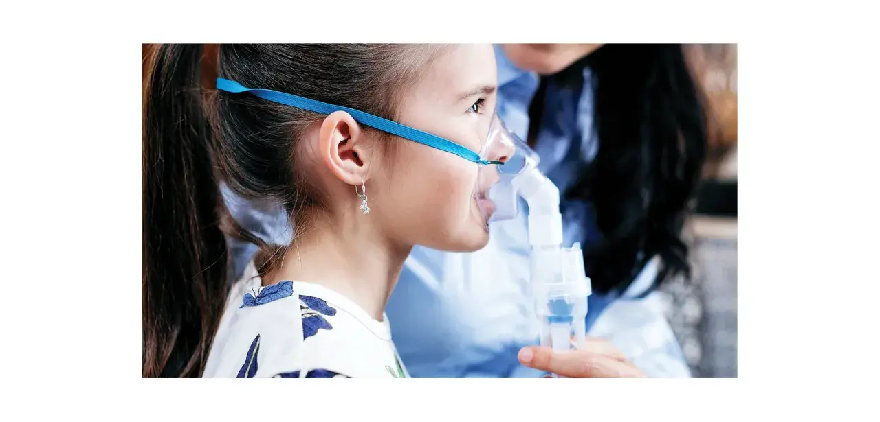 Dziewczynka z maską inhalatora Microlife. W dolnej części widać pojemnik, do którego wlewa się lek.