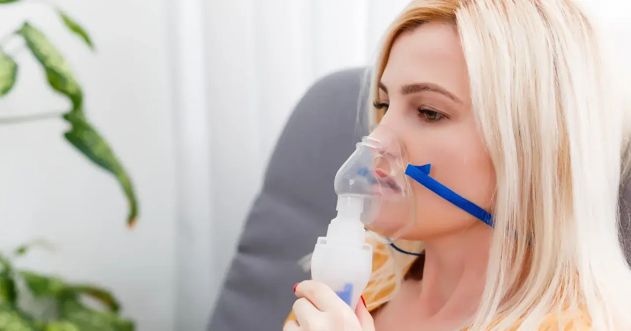 Kobieta z maską inhalacyjną na twarzy. Choć inhalacje solą fizjologiczną są bezpieczne, warto znać potencjalne skutki uboczne.