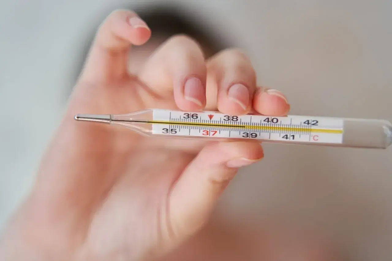 Dłoń trzyma termometr, pokazując, jak zmierzyć temperaturę. Widoczna jest skala od 35 do 42 stopni Celsjusza.