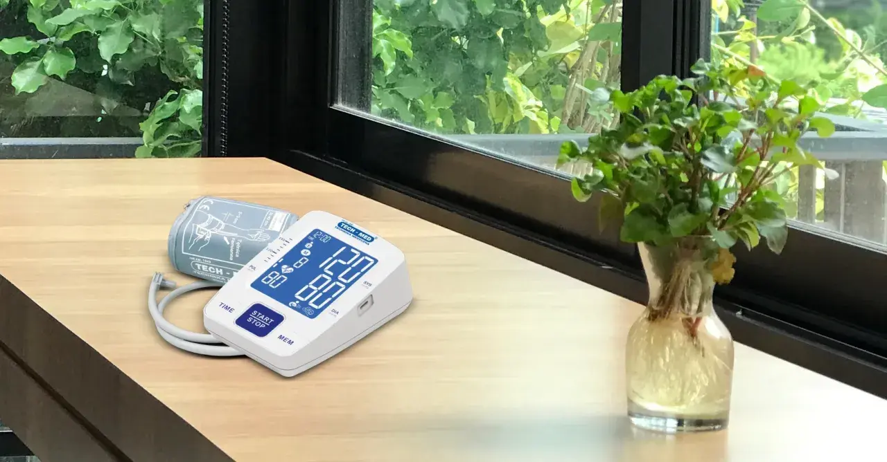 Cyfrowe symbole na ciśnieniomierzu TECH-MED pokazują odczyt 120/80. Obok leży mankiet.