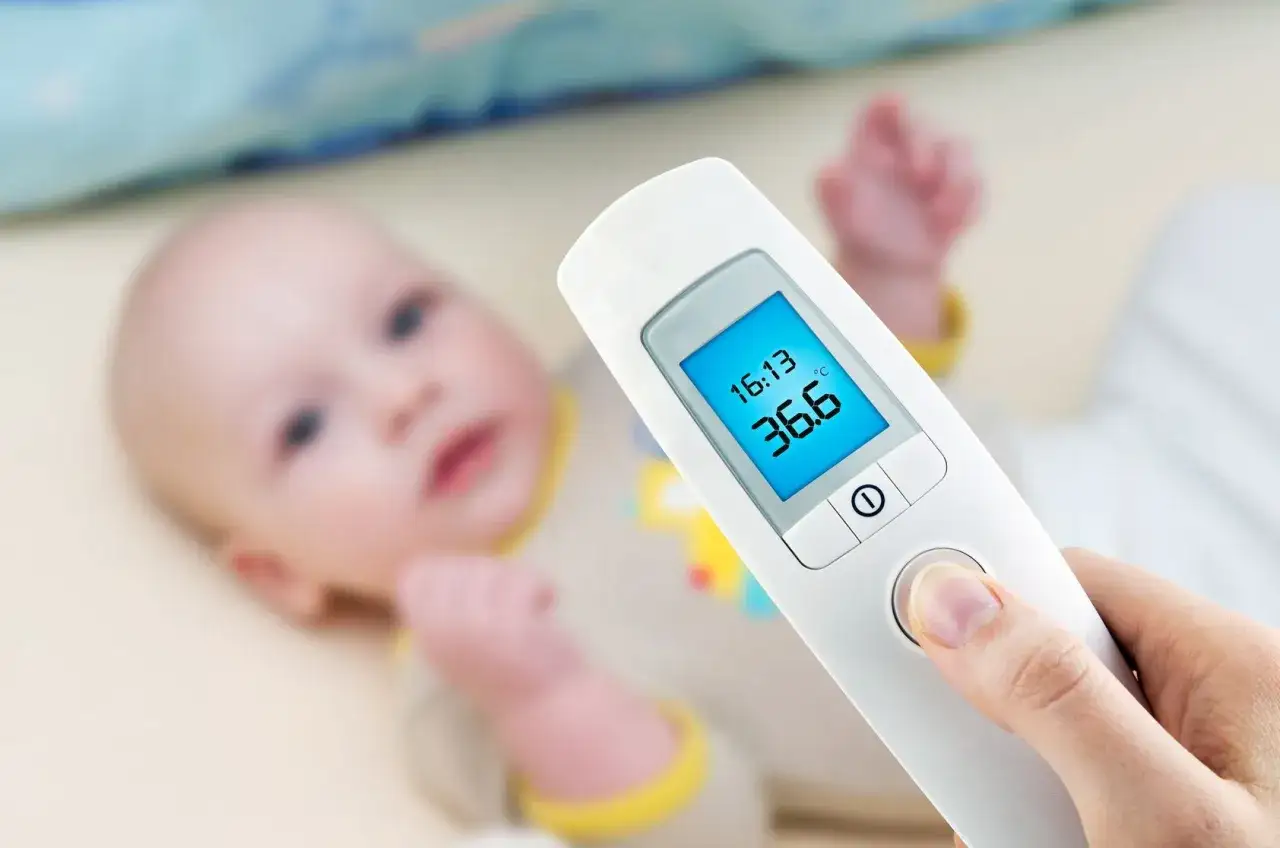 Termometr dla niemowlaka pokazuje 36.6°C. Maluch leży spokojnie, a rodzic sprawdza jego temperaturę.