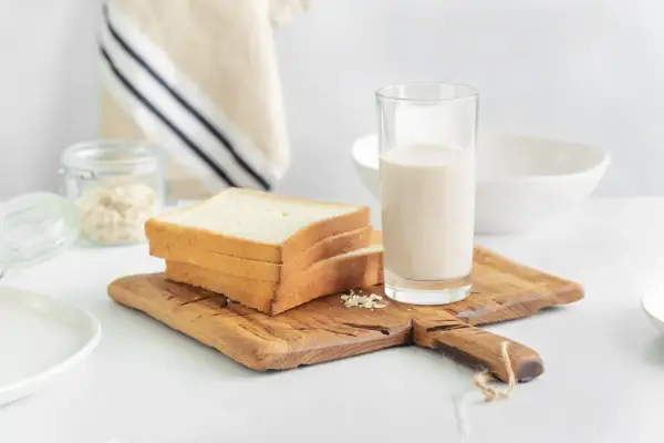 Kanapki z białego pieczywa i szklanka mleka na desce. Czy w mleku jest gluten? Pytanie o składniki śniadania.