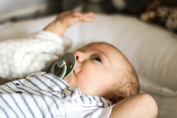 Niemowlę z zielonym smoczkiem, leżące na białej poduszce. Spokojna buzia i lekko uniesiona rączka świadczą o prawidłowej temperaturze u niemowlaka na czole.