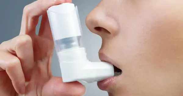 Dłoń trzyma biały inhalator na astmę, który osoba wkłada do ust.