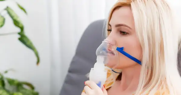 Kobieta z maską inhalacyjną na twarzy. Choć inhalacje solą fizjologiczną są bezpieczne, warto znać potencjalne skutki uboczne.